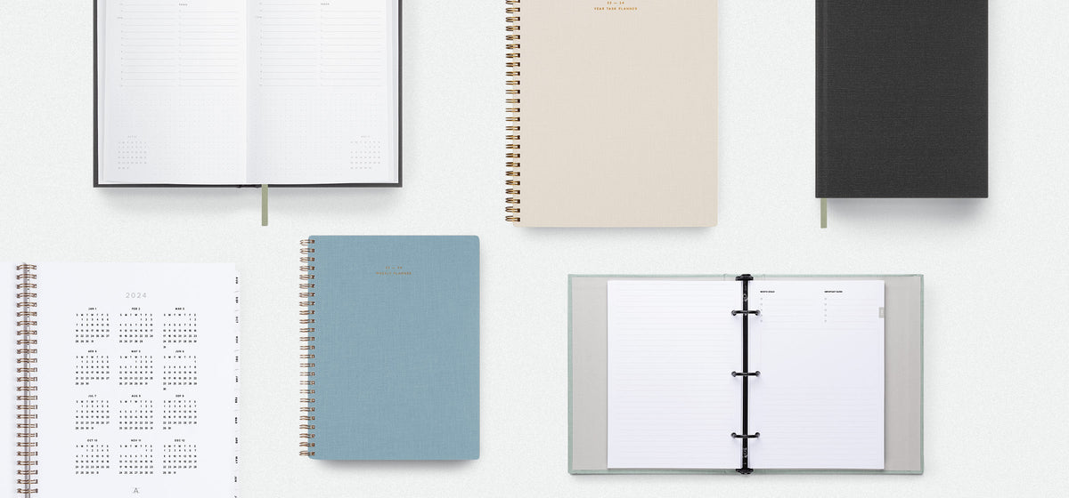 A flatlay shows the 23-24 Planner & Calendar collection against a gray background. Some planners are open while other remain closed.