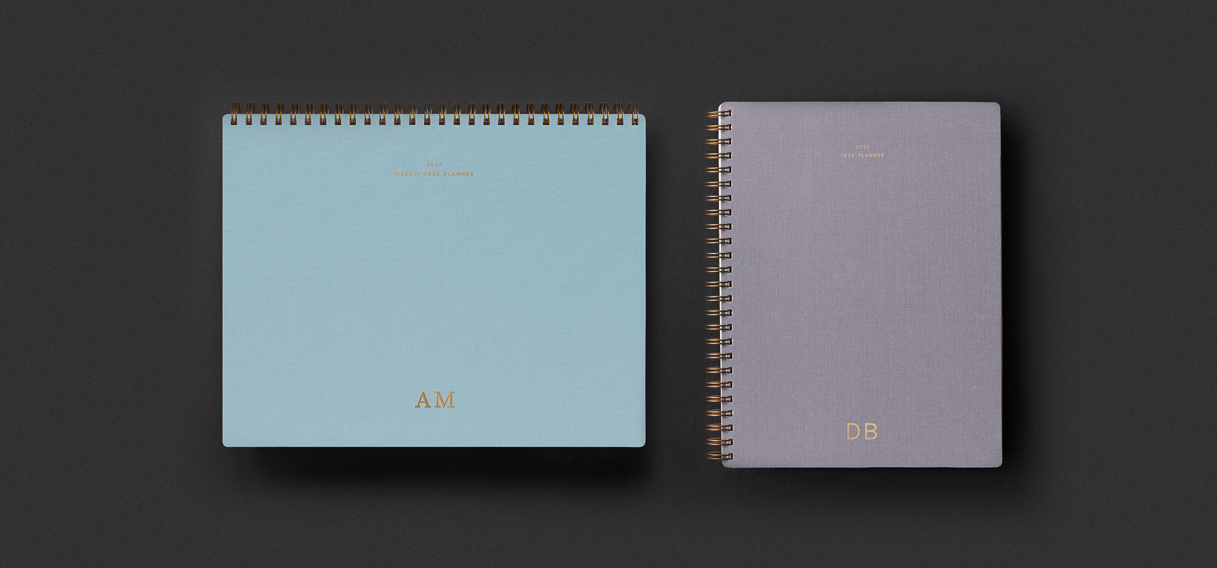 The Weekly Task Planner in Sky Blue and Compact Task Planner in Lavender Gray sit against a dark green background
